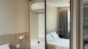 A hotel room with a bed, bedside table, and a large mirror reflecting the room.