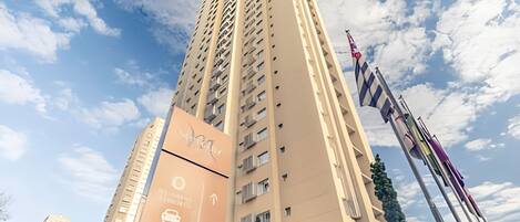 Un edificio alto y color beige con una fachada singular y varios balcones. Hay banderas en el lado derecho del edificio.