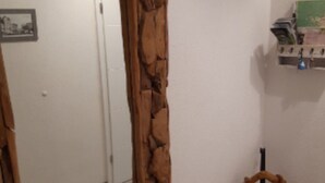 A room with a rustic wooden-framed mirror, a small wooden bench with a fur throw, and a wall-mounted shelf with books and a small decorative item. - Apartment Wurmbergblick (Braunlage)