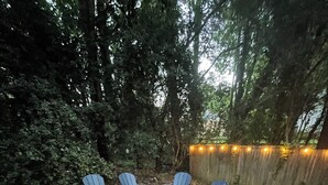 Een rond zitgedeelte met Adirondack-stoelen rond een vuurkorf, omgeven door een houten hek en bomen.