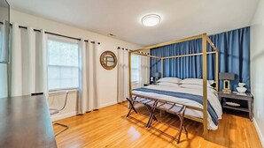 Een slaapkamer met een hemelbed, houten vloeren, een bureau en een nachtkastje met lamp.