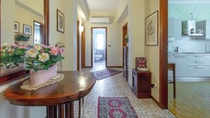 A hallway with a wooden table, a potted plant, and a mirror. There is a door leading to a bathroom and a kitchen area. - Le bouganville, 3 bedrooms Apt, city center and parking place (Desenzano del Garda)
