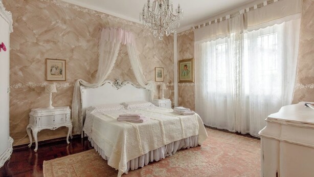 A bedroom with a four-poster bed, a chandelier, and a large window with sheer curtains. - Le bouganville, 3 bedrooms Apt, city center and parking place (Desenzano del Garda)