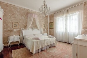 A bedroom with a four-poster bed, a chandelier, and a large window with sheer curtains.