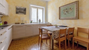 A kitchen with a dining table, chairs, a window, and a painting on the wall. - Le bouganville, 3 bedrooms Apt, city center and parking place (Desenzano del Garda)