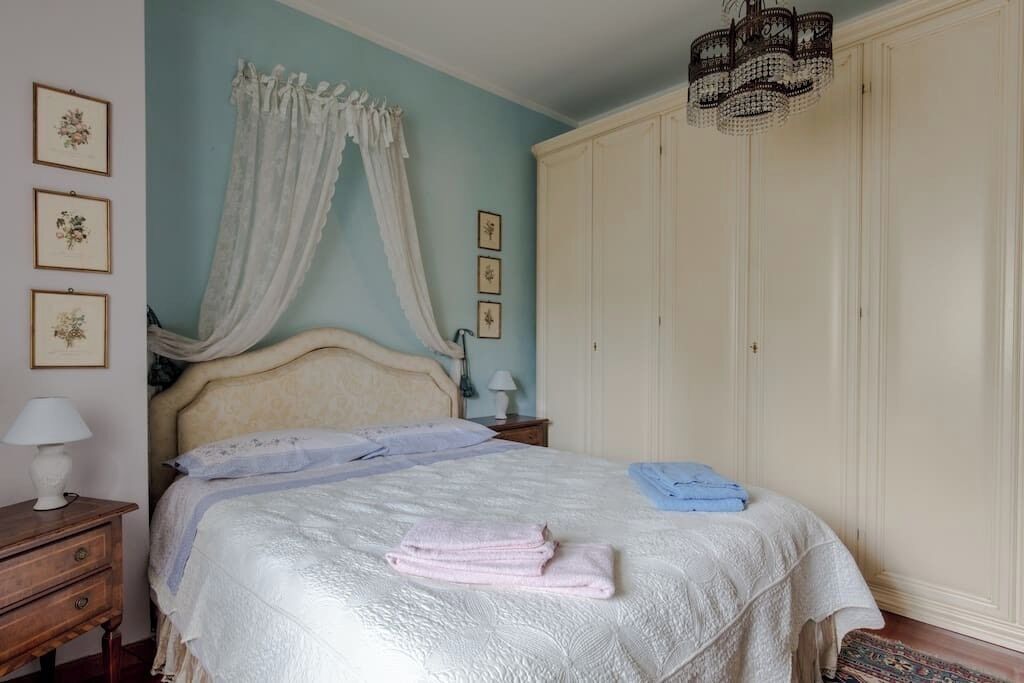 Een slaapkamer met een bed, nachtkastje, garderobe en een kroonluchter.