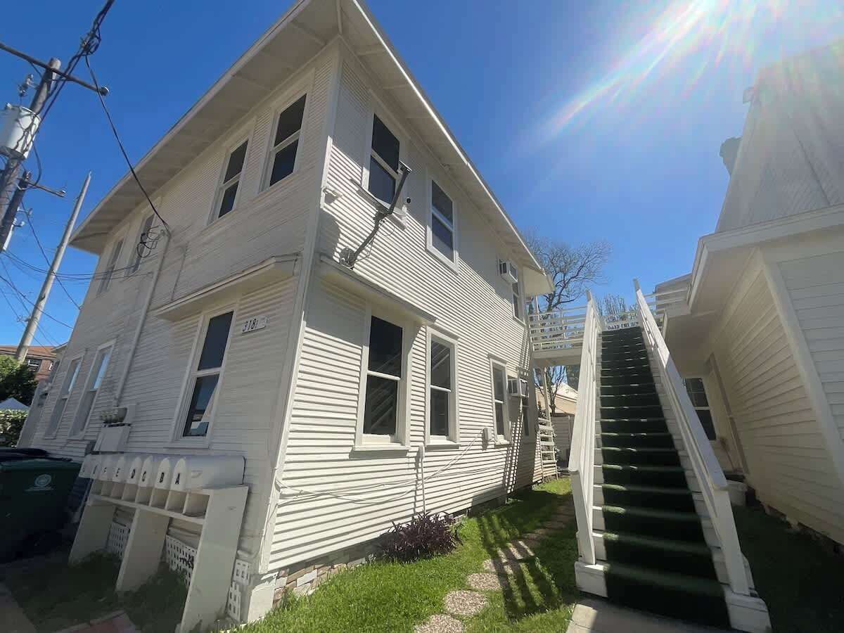 A two-story white house with a front porch and a staircase leading to the second floor.