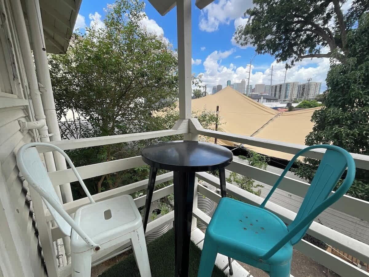 Een balkon met een kleine tafel en twee stoelen, met uitzicht op een stadsgezicht met gebouwen en bomen.