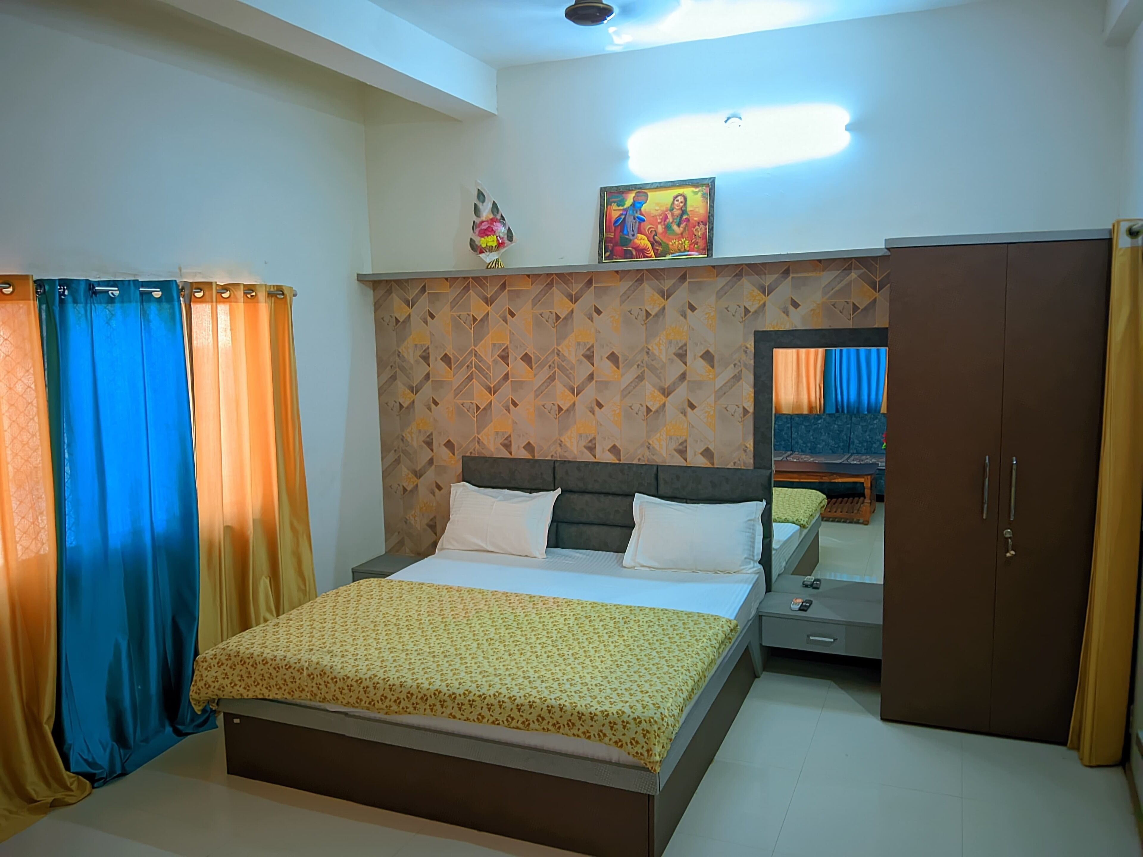 A bedroom with a bed, a wardrobe, a mirror, and a wall with a geometric pattern.
