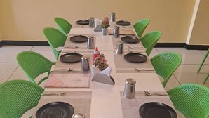 A rectangular dining table with green chairs, set with plates, cutlery, and condiments. - Hotel divine and restaurant (Pratapgarh)