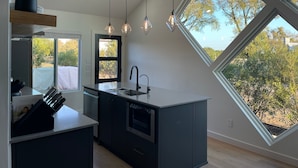 Een moderne keuken met een groot raam, hangende lampen en een inbouwvaatwasser.