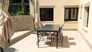An outdoor patio with a dining table and chairs, surrounded by a stone wall and covered by a beige umbrella. - Le Charme Des Cerisiers - 3-star family B&B with private spa and garden.  (Bouvigny-Boyeffles)