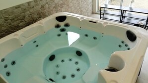 A hot tub with multiple jets, a stone wall, and a view of an outdoor area through a glass door. - Le Charme Des Cerisiers - 3-star family B&B with private spa and garden.  (Bouvigny-Boyeffles)