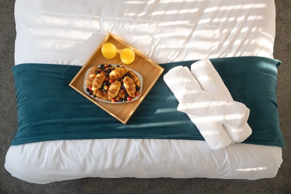 A bed with a teal and white pillow, a tray with croissants and berries, and a white towel.