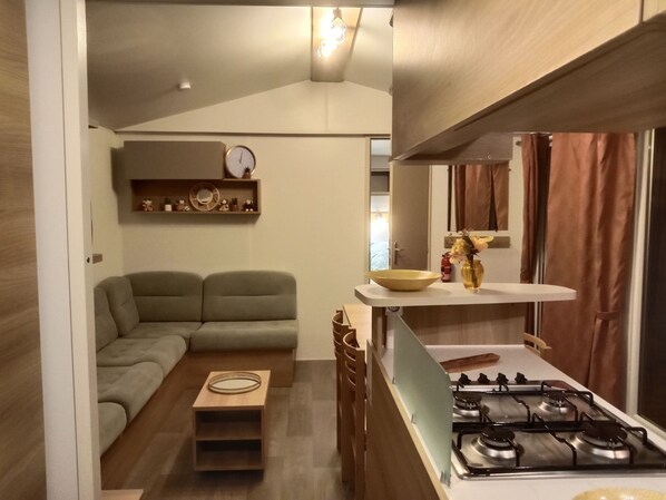 Un espacio habitable compacto con sofá, una mesita, estufa a gas y estante con objetos decorativos.