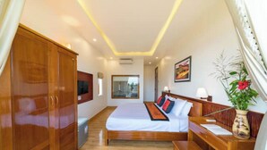 A bedroom with a large bed, wooden wardrobe, bedside table, and a desk with a chair.