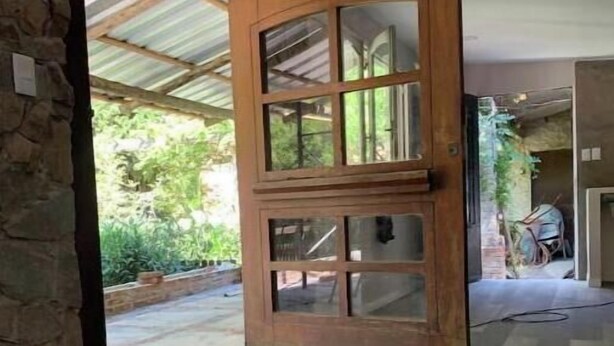 A room with a large wooden door leading to an outdoor area. The room has a stone wall and a tiled floor.
