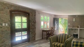 A living room with a stone wall, a dining area with a table and chairs, and a kitchen area with a sink and cabinets.