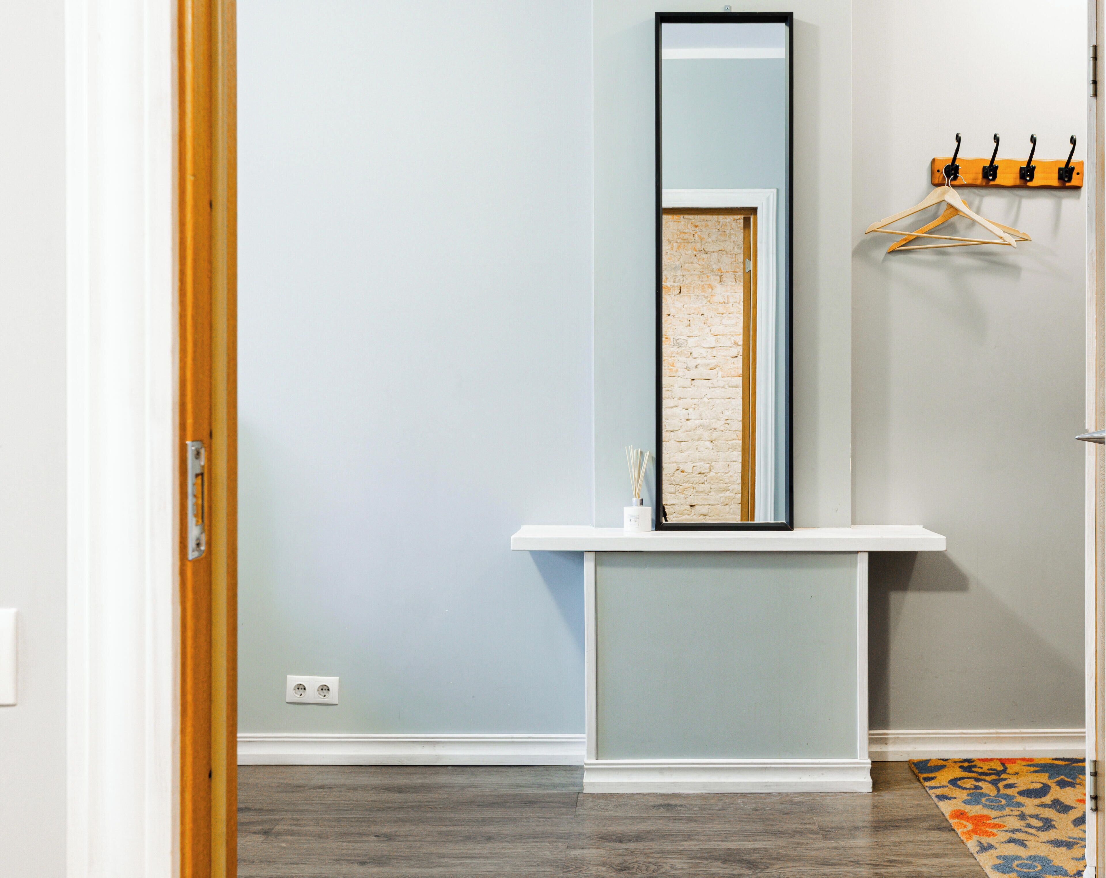 A room with a white vanity, a mirror, a hanging wooden coat rack, and a patterned rug.