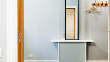 A room with a white vanity, a mirror, a hanging wooden coat rack, and a patterned rug.