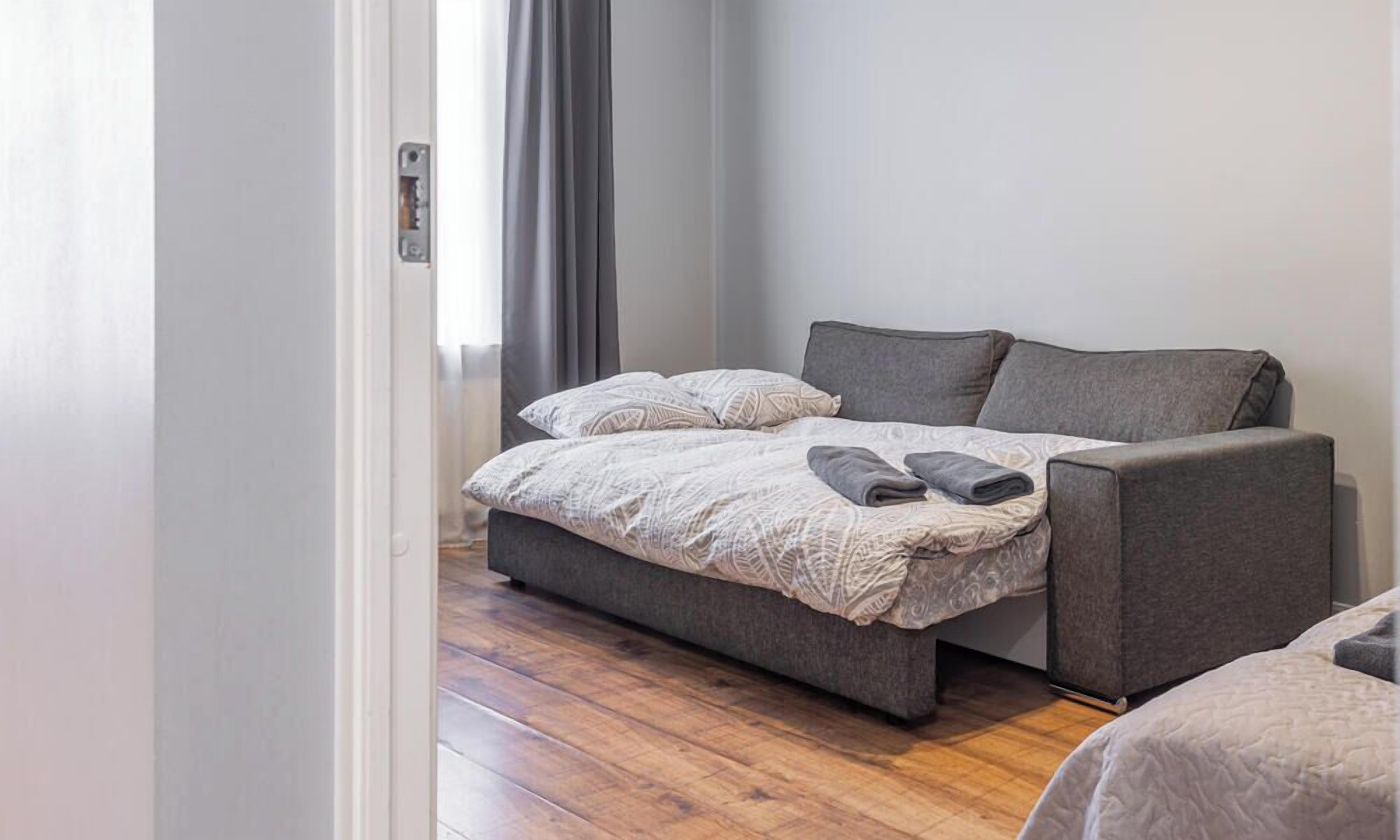 Une chambre avec un lit, un canapé, une fenêtre avec des rideaux et un plancher en bois.