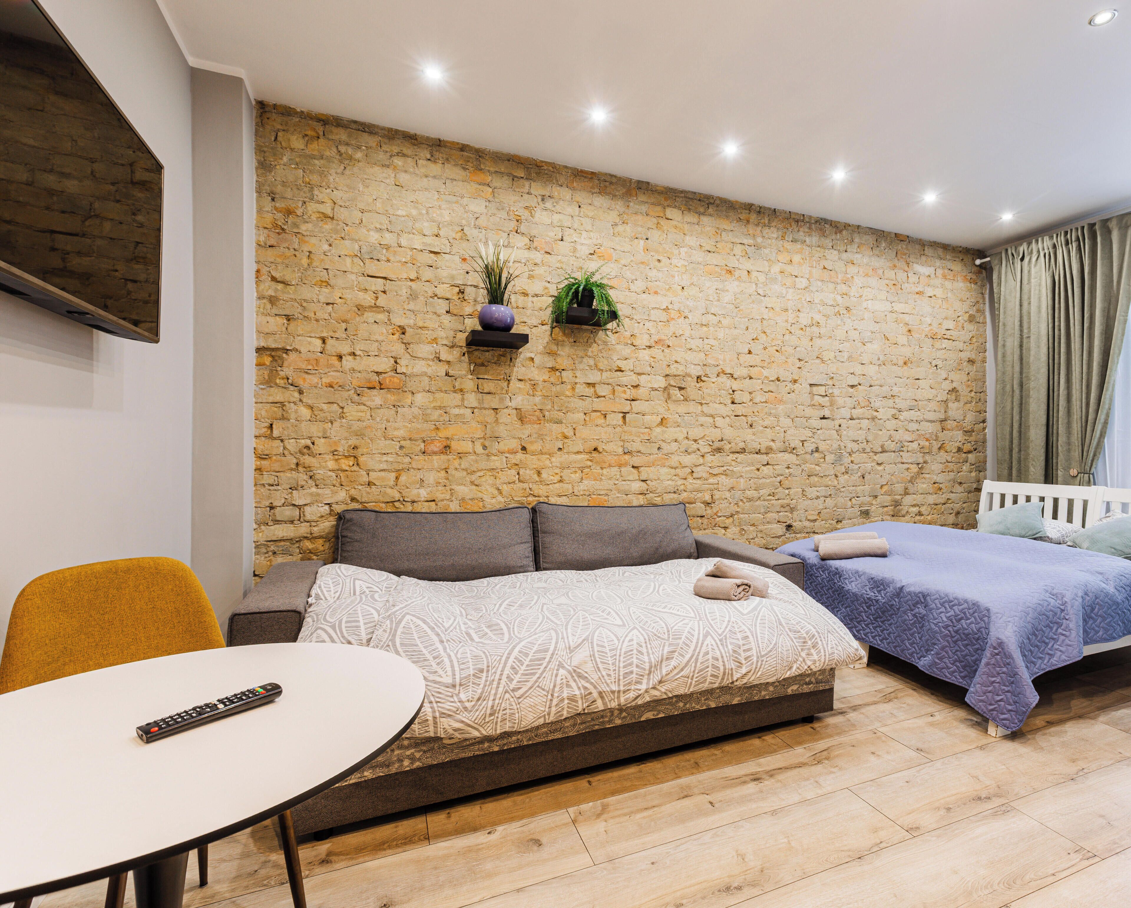 Ein modernes Zimmer mit Steinwand, Schlafsofa, Einzelbett, Tisch und Stuhl.