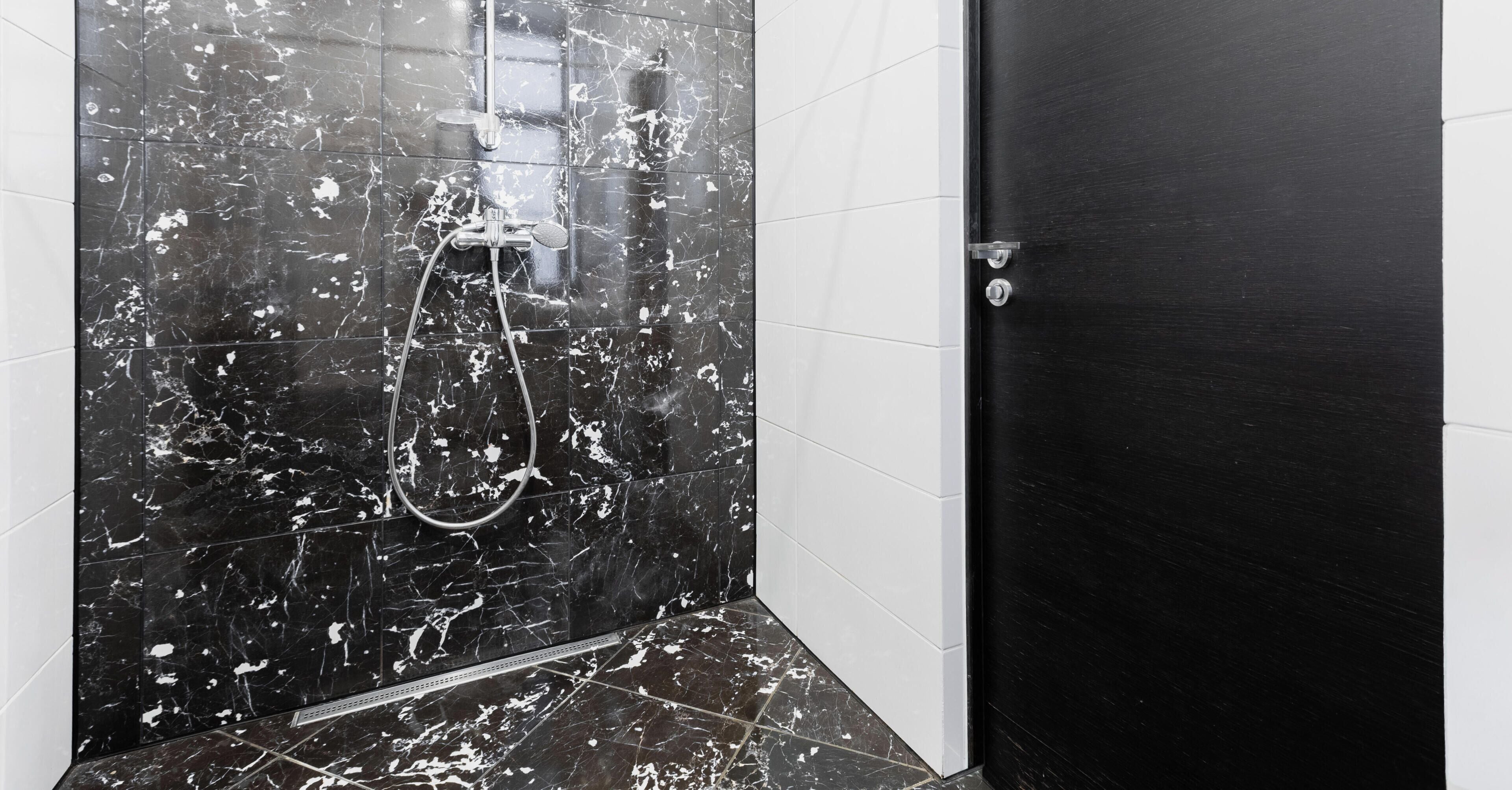 A bathroom with black marble tiles, a shower, and a black door.