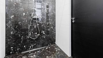 A bathroom with black marble tiles, a shower, and a black door.