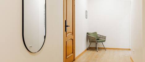 A hallway with a wooden door, a mirror, and a chair.