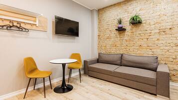 A room with a stone wall, a sofa, two chairs, a small table, and a mounted TV.