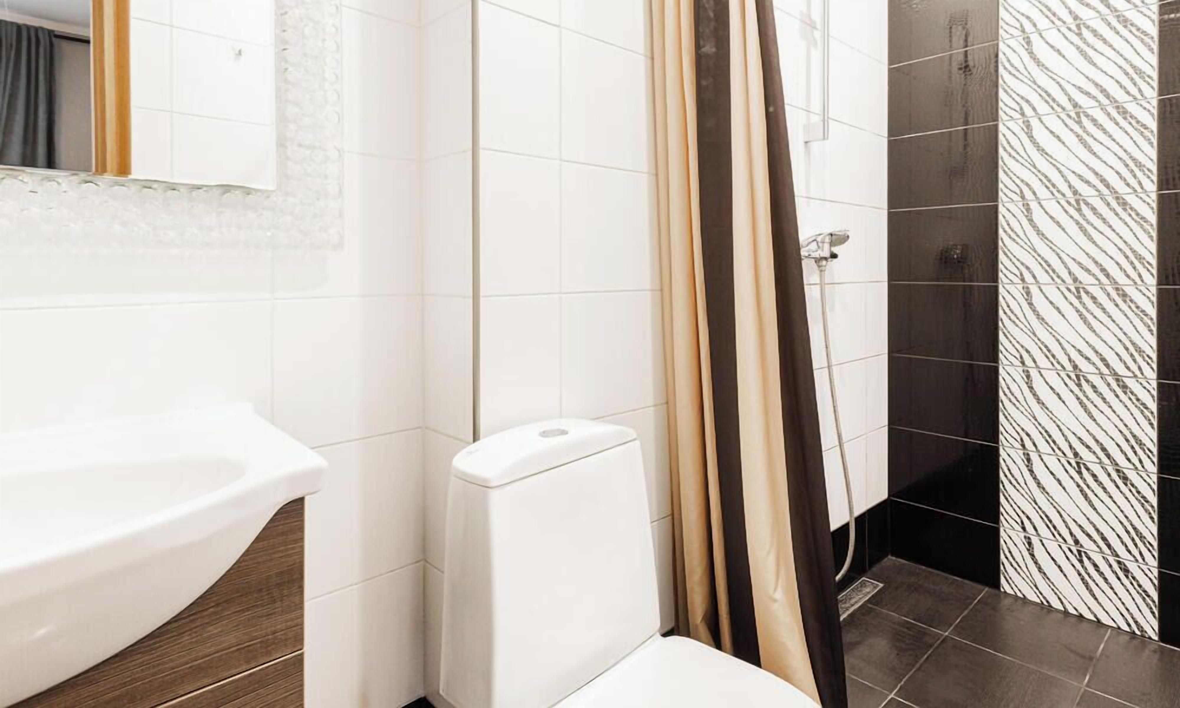 A bathroom with a white sink, a toilet, and a shower area with a patterned wall.