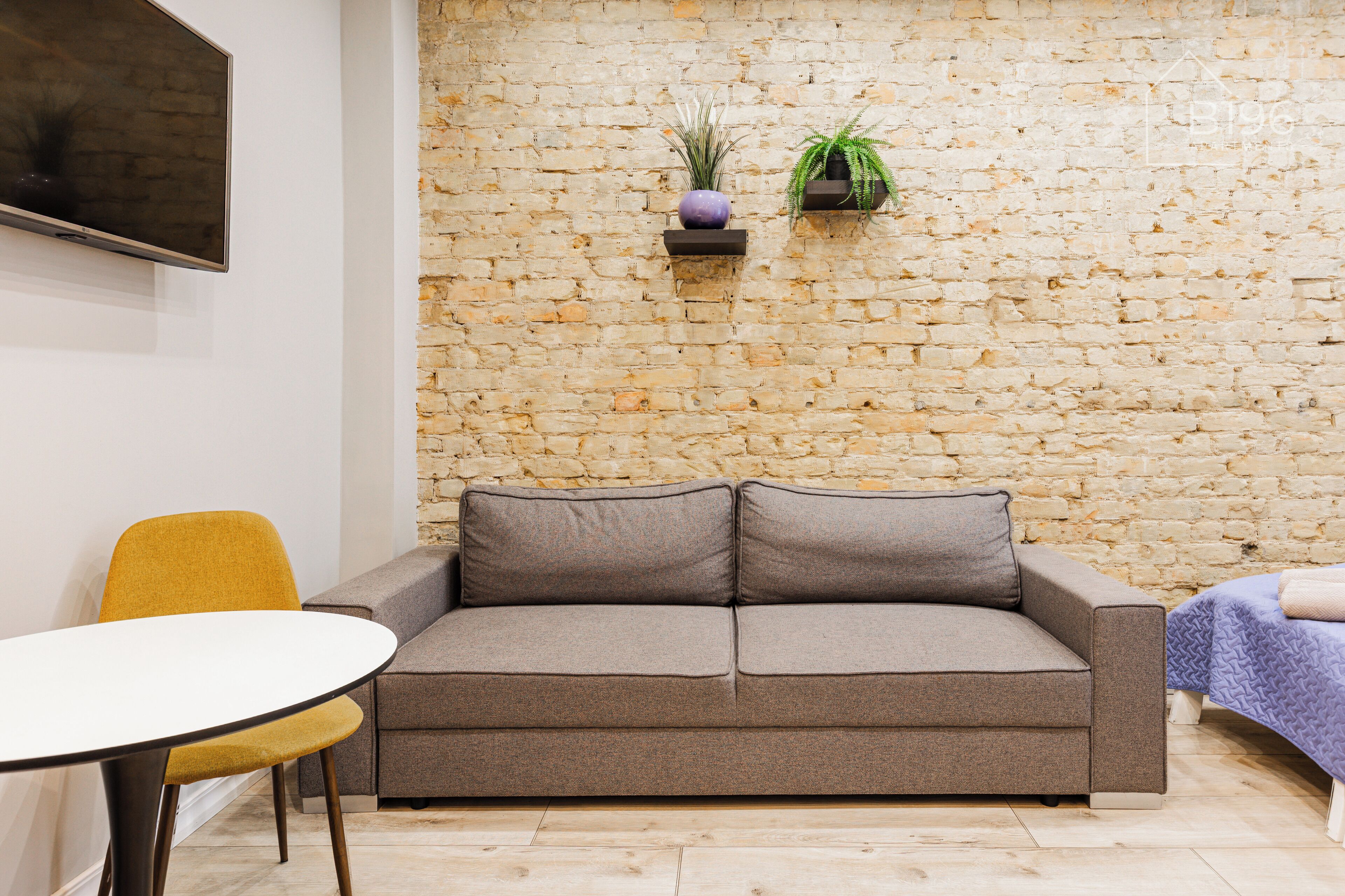 Una habitación con pared de piedra, un sofá, una silla amarilla y una pequeña mesa.