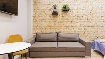 Una habitación con pared de piedra, un sofá, una silla amarilla y una pequeña mesa.