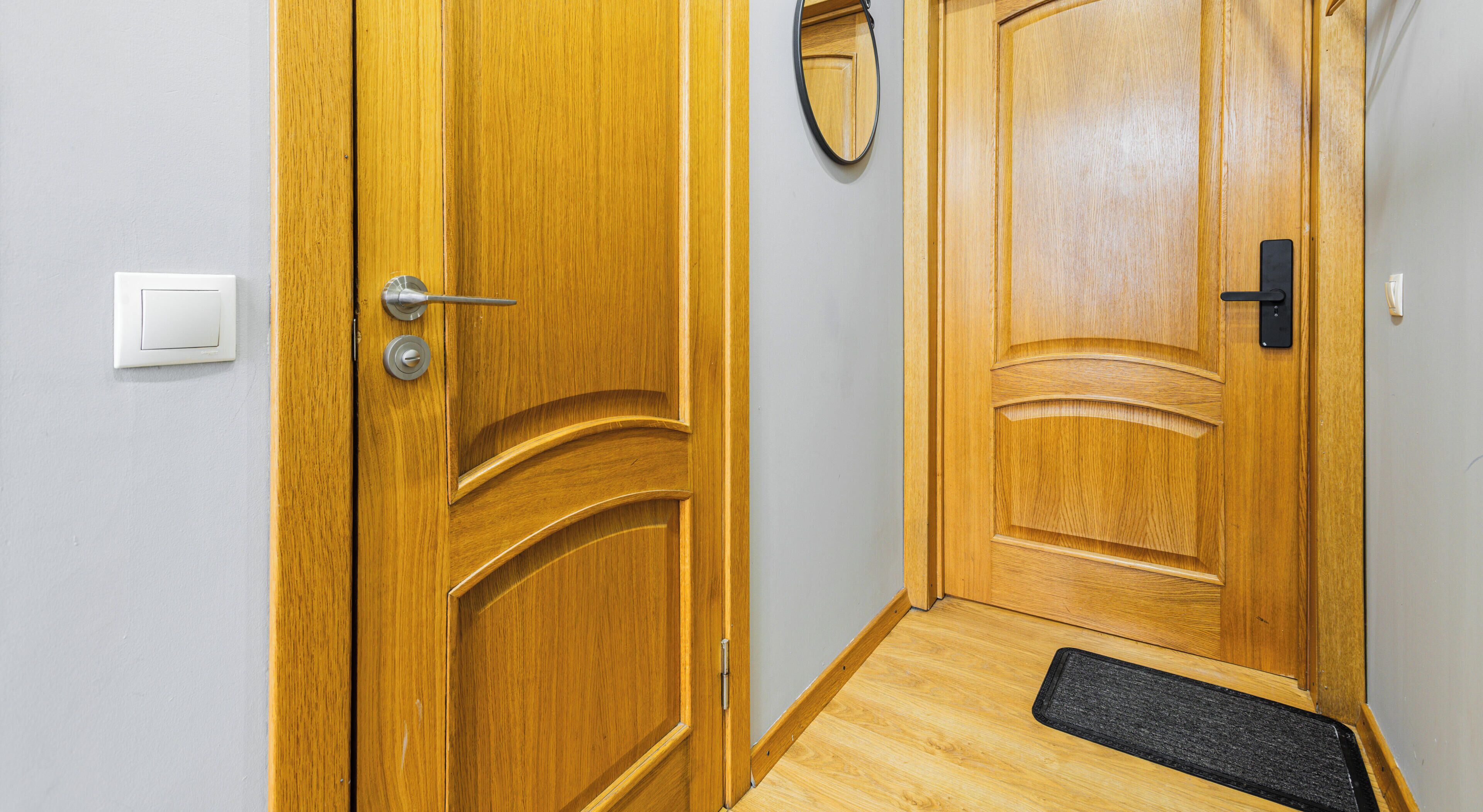 A wooden door with a handle and a keyhole, a doormat, and a light switch on the wall.