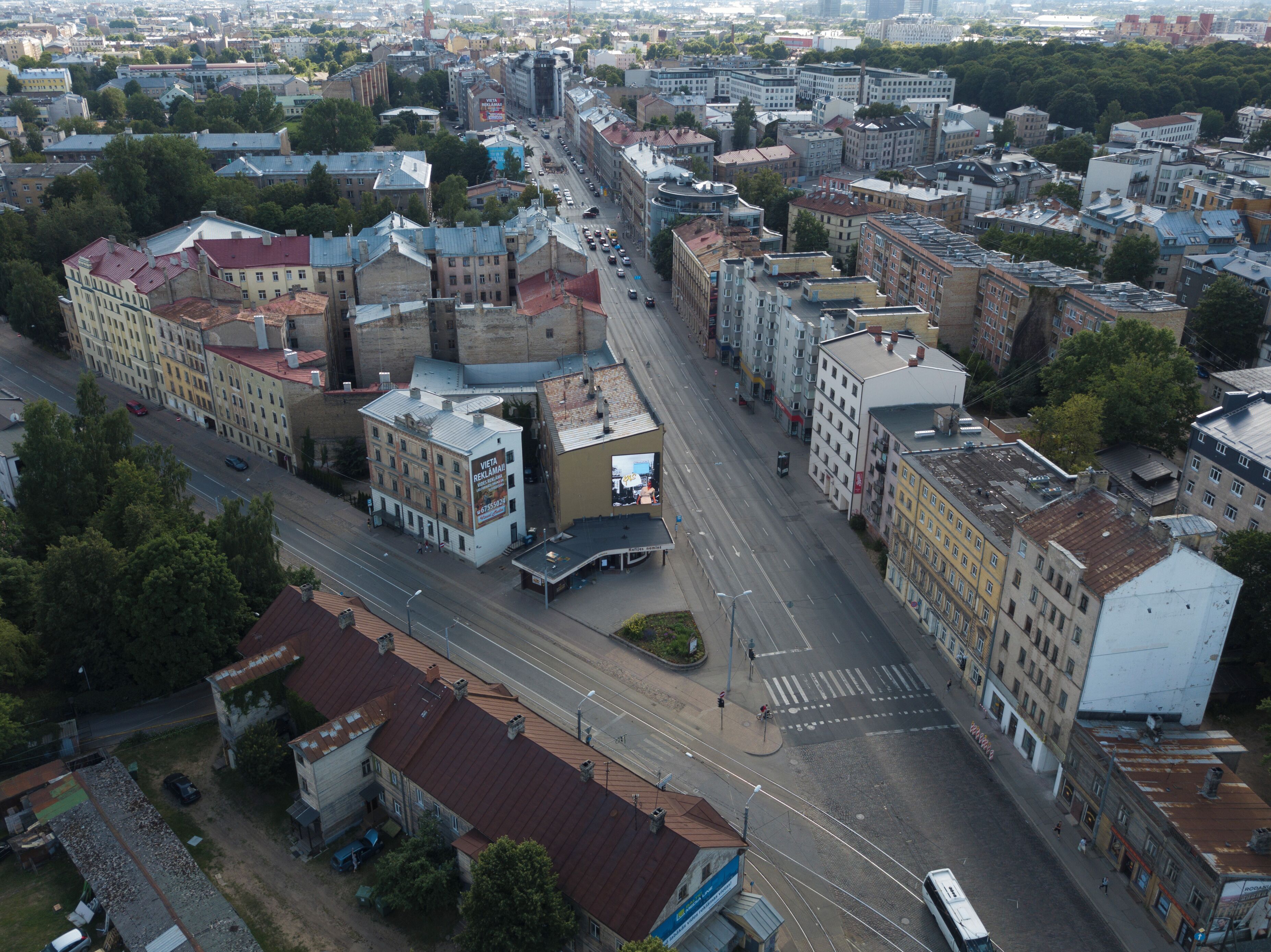 Luchtbeeld van een stadsgezicht met een mix van oudere en moderne gebouwen, een brede straat en een tramlijn.