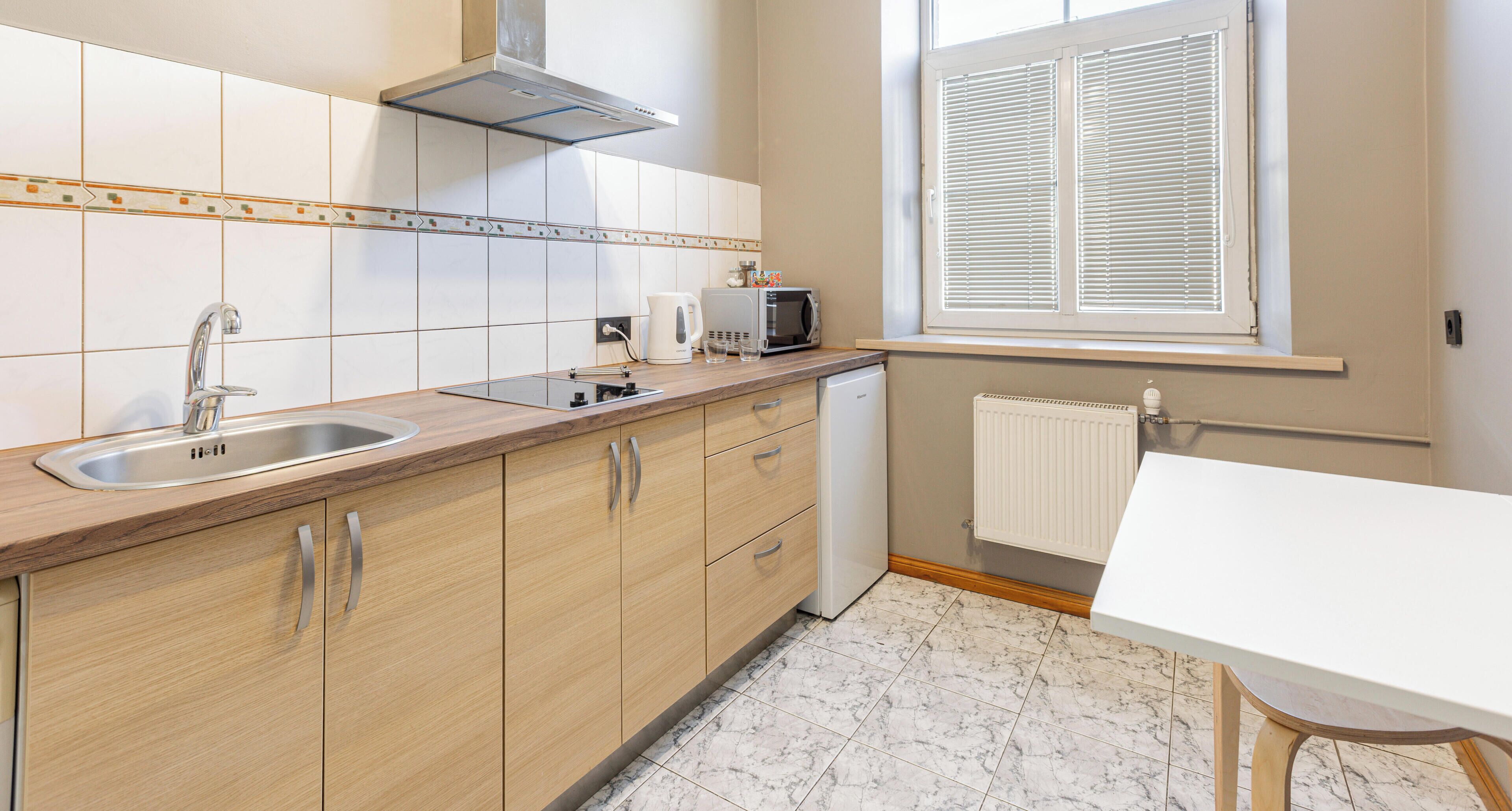 A kitchen with a sink, stove, microwave, and a window with blinds.