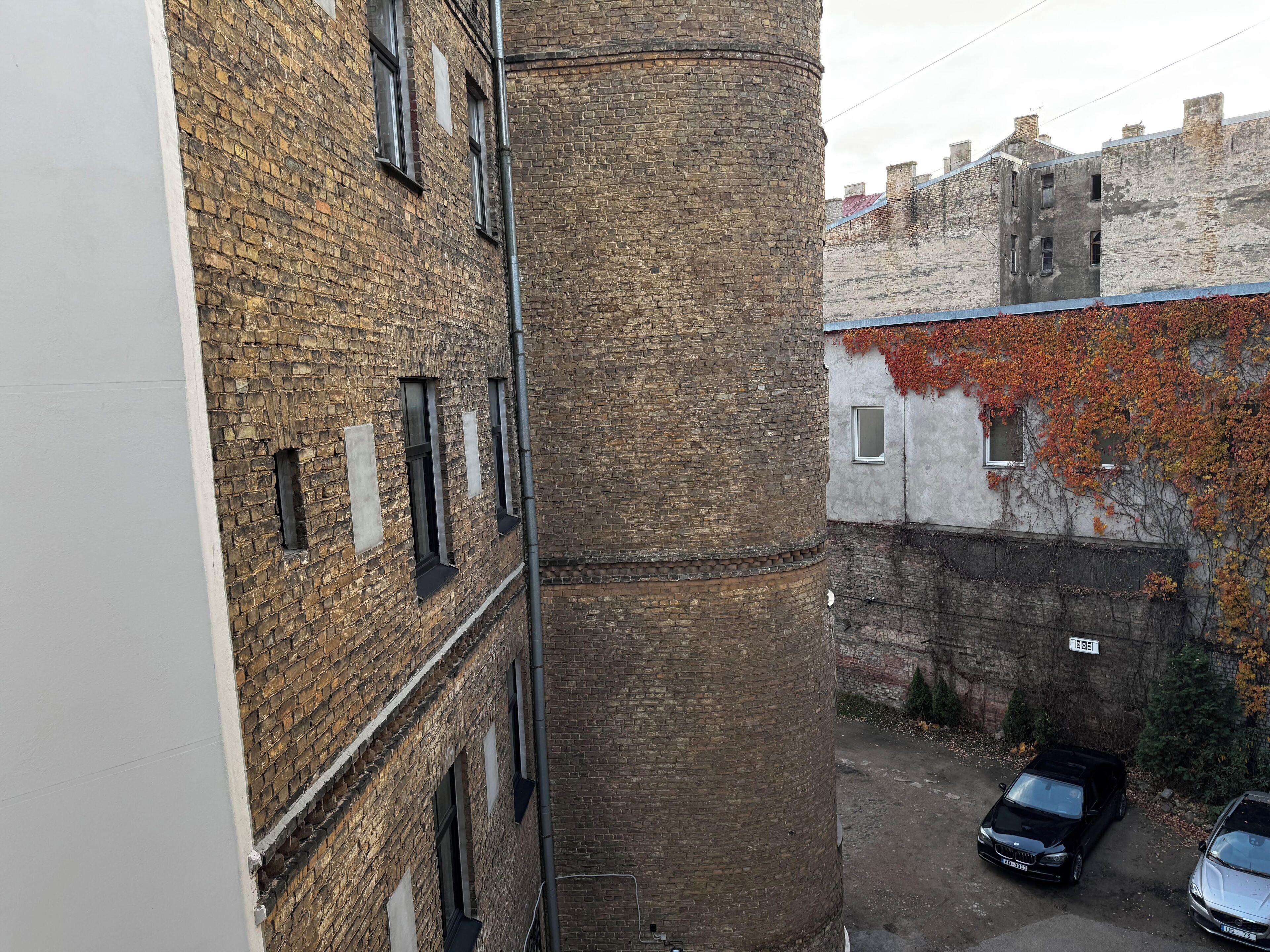 Un callejón estrecho con edificios de ladrillo, una estructura cilíndrica y coches estacionados.