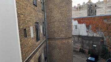 Un callejón estrecho con edificios de ladrillo, una estructura cilíndrica y coches estacionados.
