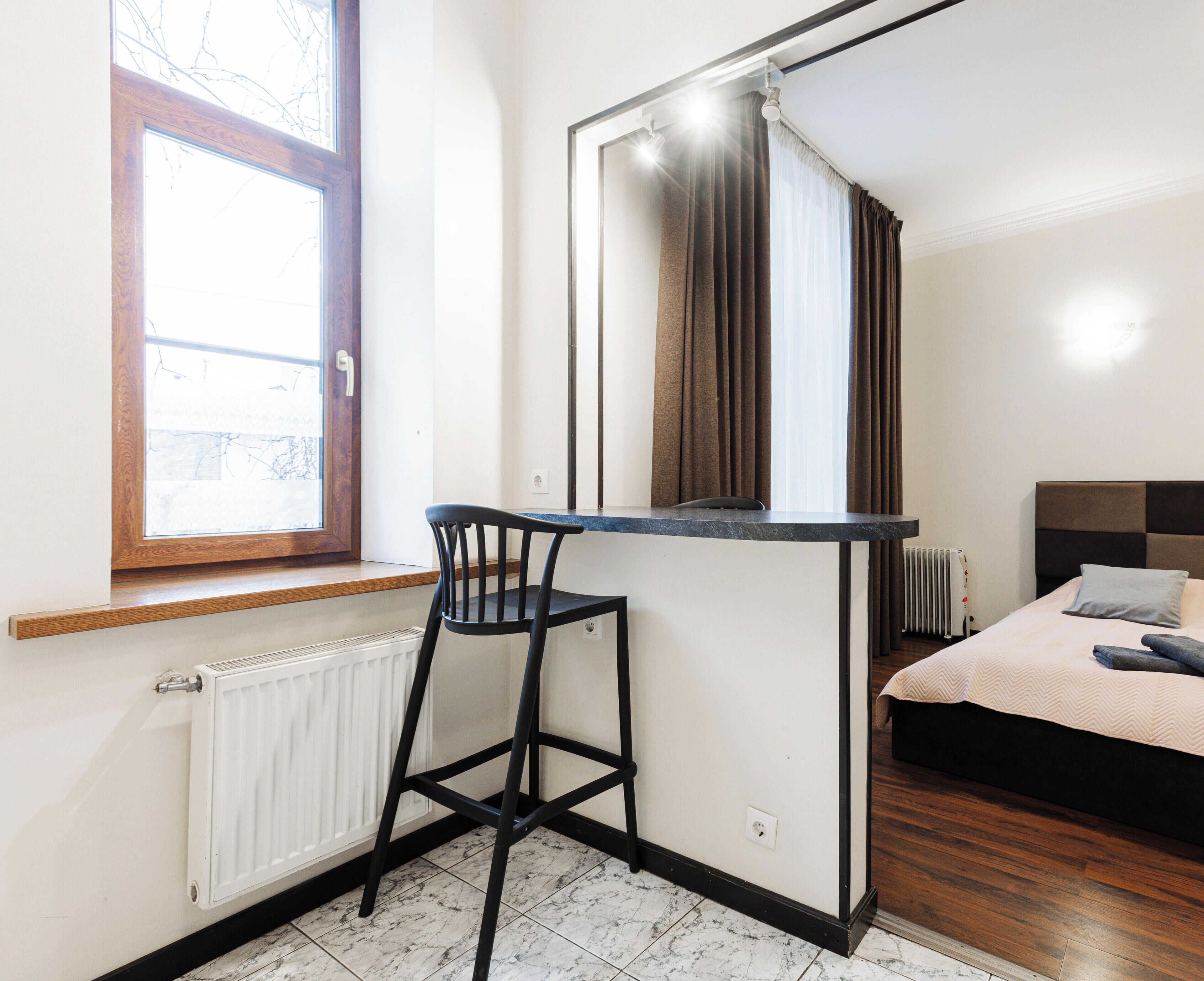 Una habitación pequeña y moderna con una sola ventana, un radiador, una cama y una zona de bar.