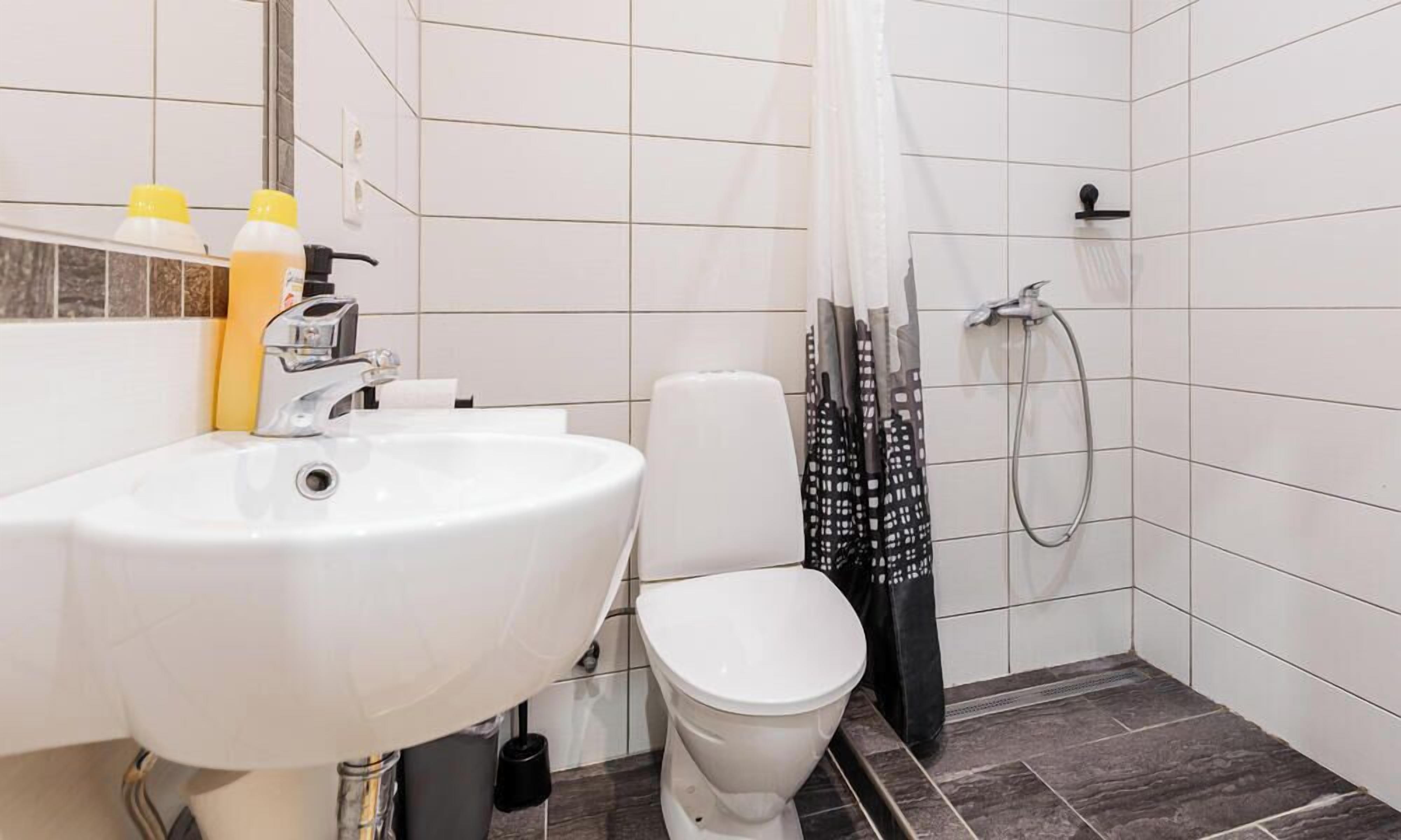 Baño con lavamanos, inodoro y zona de ducha blancos.