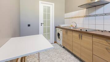 Een keuken met een wasmachine, houten kastjes, een wit aanrechtblad en een betegelde spatwand.