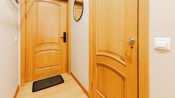 A wooden door with a doorknob and a handle, a small mirror on the wall, and a light switch on the wall.