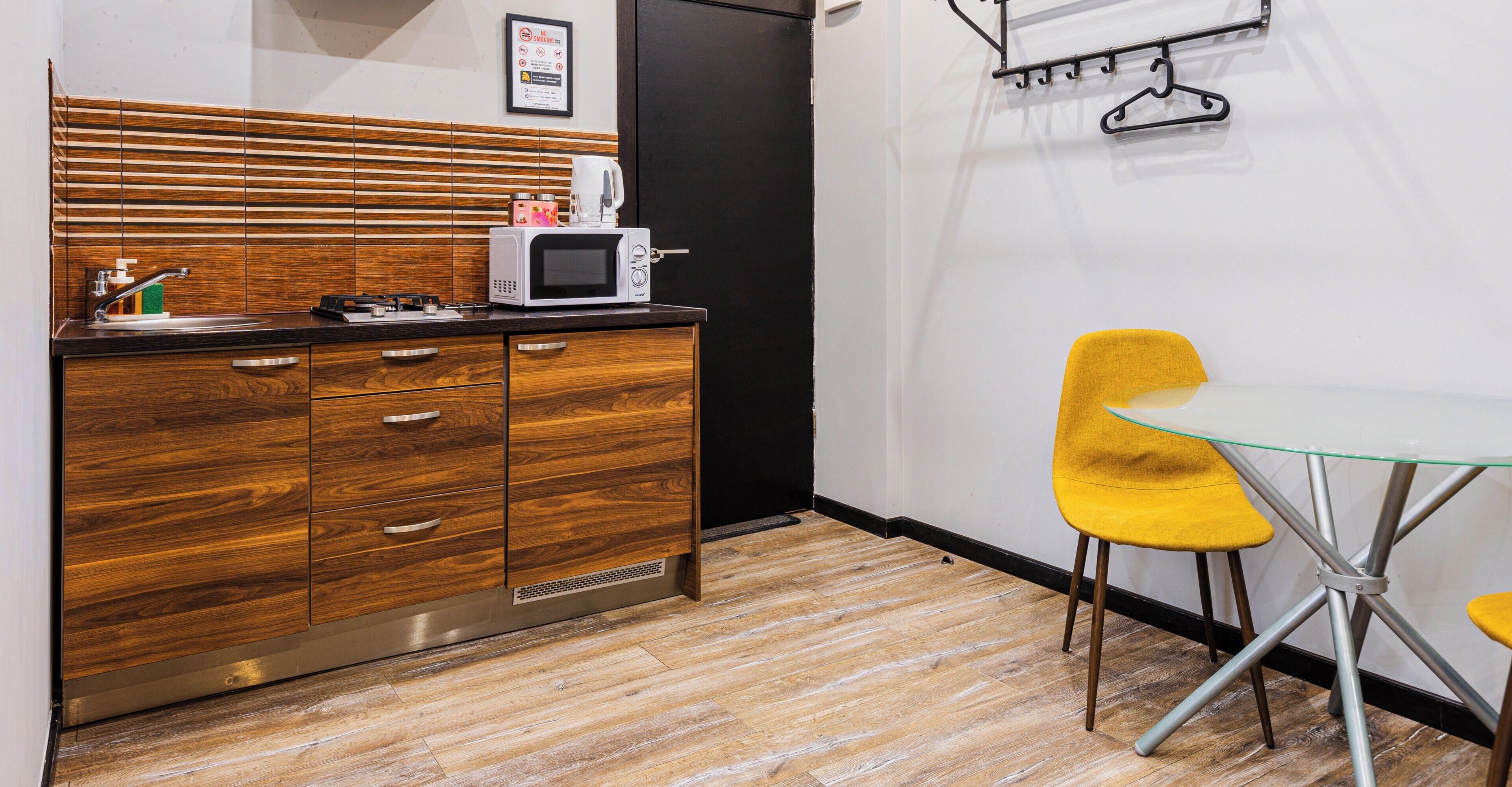 A compact kitchenette with a microwave, a coffee maker, and a small sink. There is a yellow chair and a glass table.