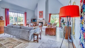 A spacious living room with a high ceiling, a fireplace, and a large window with curtains. - La Rocherie - Charmante maison avec piscine privée (Carnac)