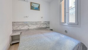 Un dormitorio con cama, aire acondicionado, un cuadro, una ventana y una mesita de noche.
