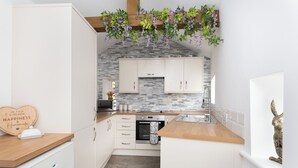 Cocina compacta con armarios blancos, salpicadero de piedra y encimera de madera.
