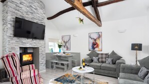 Una sala moderna con chimenea de piedra, televisor de pantalla plana, sofá, sillón a rayas y un comedor con mesa y sillas.
