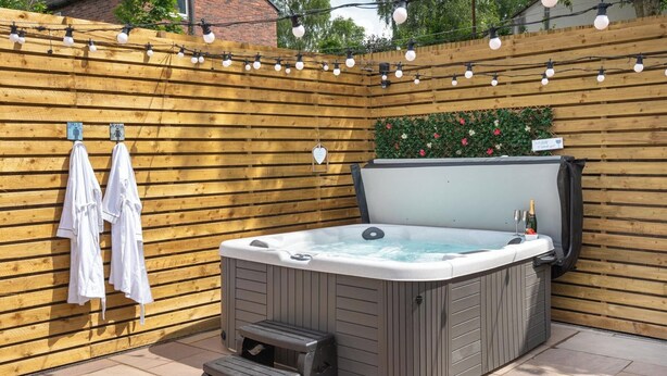Un jacuzzi con un taburete, rodeado por una valla de madera y luces colgantes.