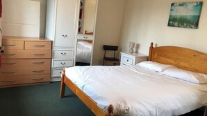 A bedroom with a wooden bed, a white wardrobe, a nightstand, and a painting on the wall. - Charming 2-bed Apartment on Exmoor (Minehead)