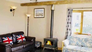 A living room with a sofa, a patterned sofa, a fireplace, a lamp, and a window with curtains. - Charming 2-bed Apartment on Exmoor (Minehead)